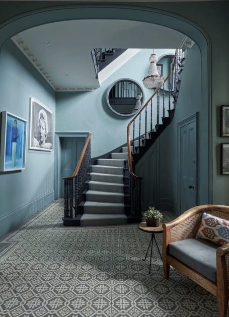 Escaliers avec rampe en bois, murs bleu clair et décoration artistique, salon à gauche.