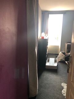 Petit couloir avec une fenêtre au fond, meuble noir et désordre au sol.