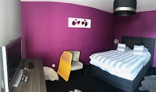Chambre moderne avec mur violet, lit, télévision et chaise jaune.