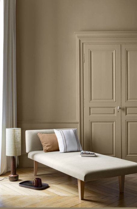 Chambre minimaliste avec un lit et une lampe, murs beiges, et lumière naturelle.