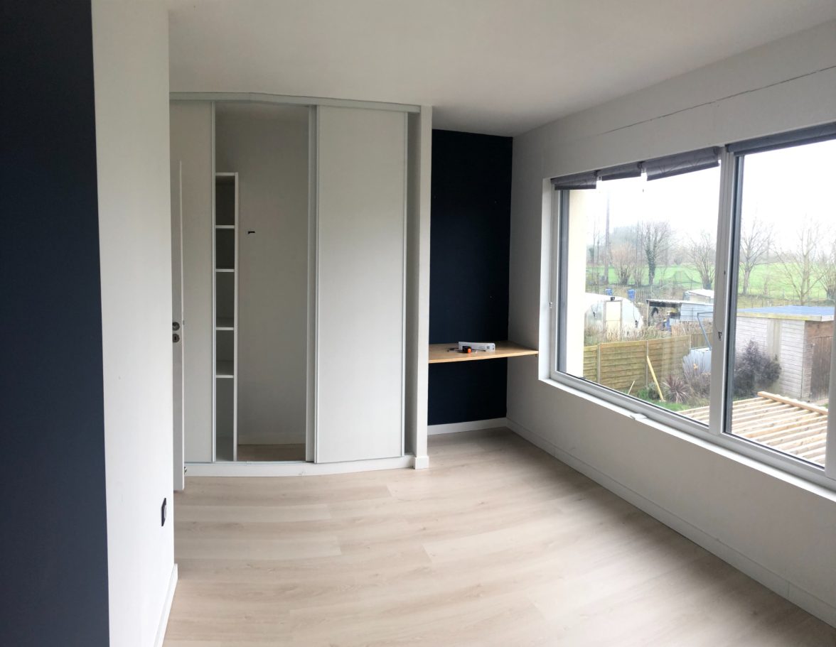 Intérieur d'une pièce avec murs clairs, un coin bureau et une fenêtre lumineuse.